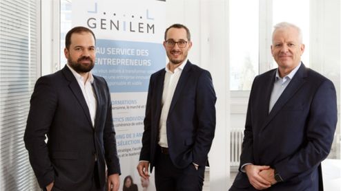Trois hommes en costume (Laurent Berney, Roland Rueff) posant devant une bannière de Genilem, organisation au service des entrepreneurs, dans un environnement professionnel lumineux.