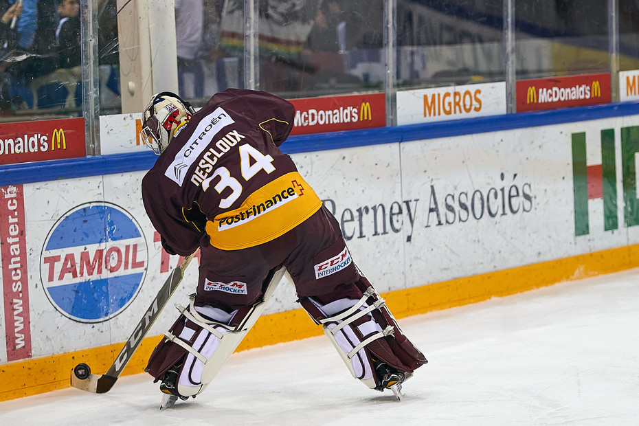 Gardien de hockey sur glace en équipement grenat (GSHC), numéro 34, en action devant la bande affichant le logo Berney Associés.