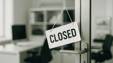 Panneau indiquant "Closed" suspendu à la poignée d'une porte vitrée donnant sur un bureau vide.